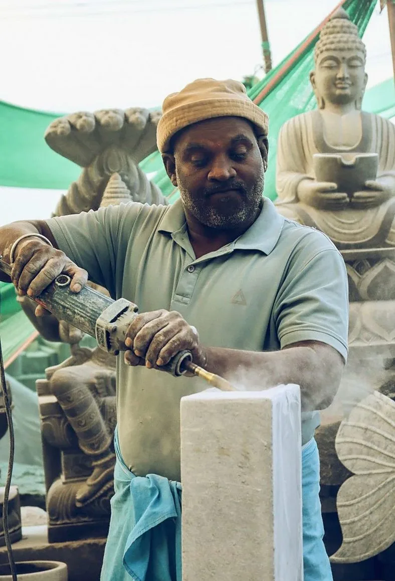 A skilled sculptor uses power tools to craft a stone sculpture in an outdoor workshop surrounded by other works.